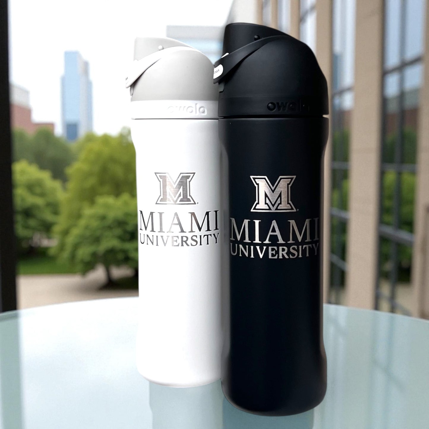 Two water bottles, one white and one black, with 'Miami University' branding on a table outdoors.