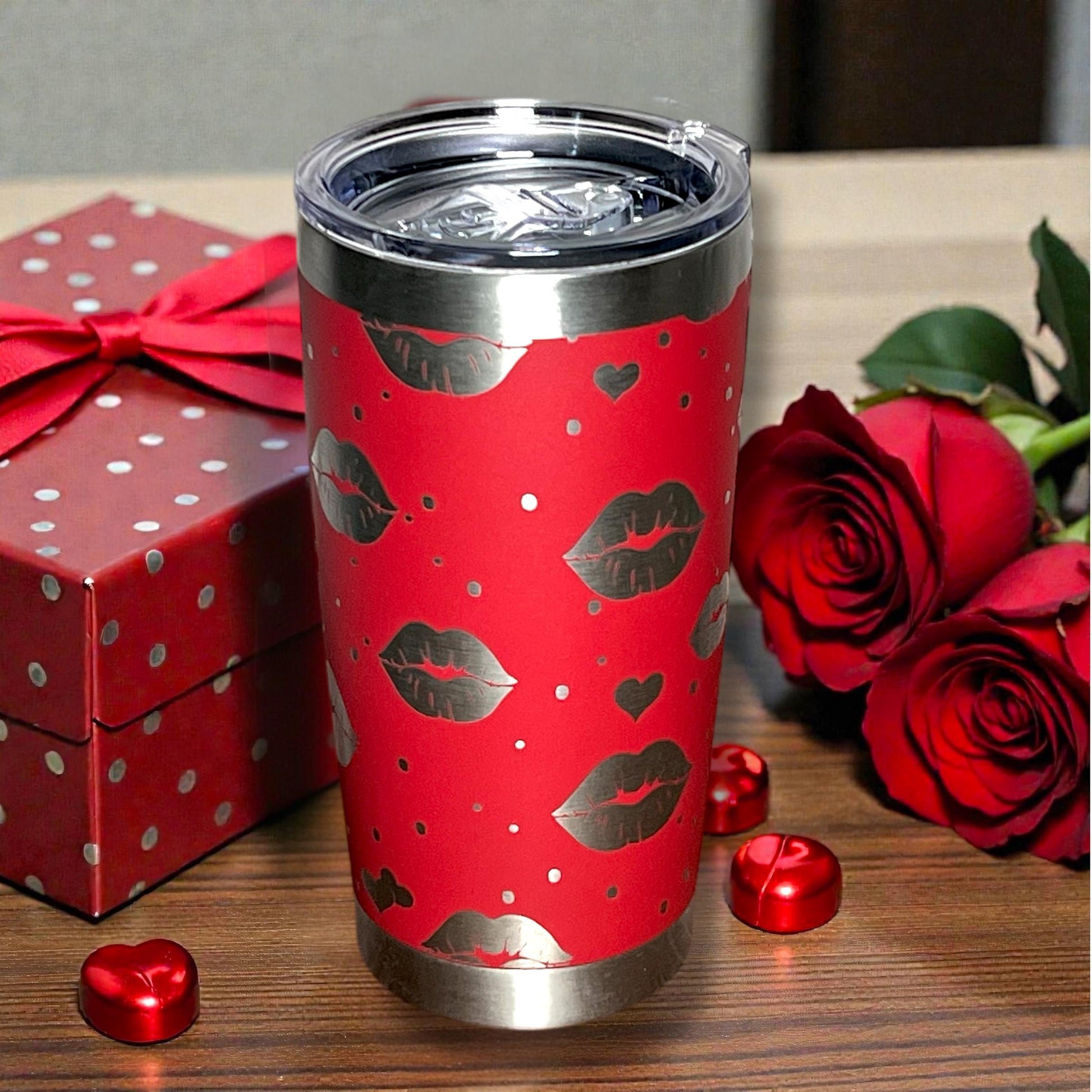 Red tumbler with lip print design on a wooden surface with red roses and a gift box.
