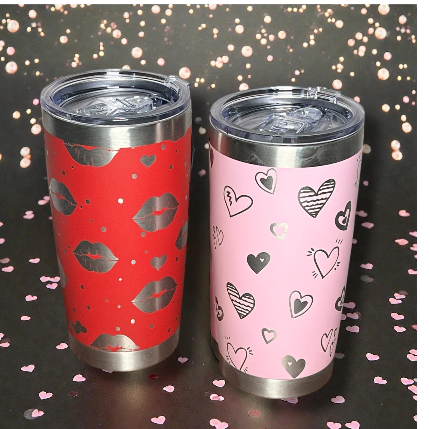 Two tumblers, one red with lip prints and one pink with heart patterns, on a dark background with confetti.
