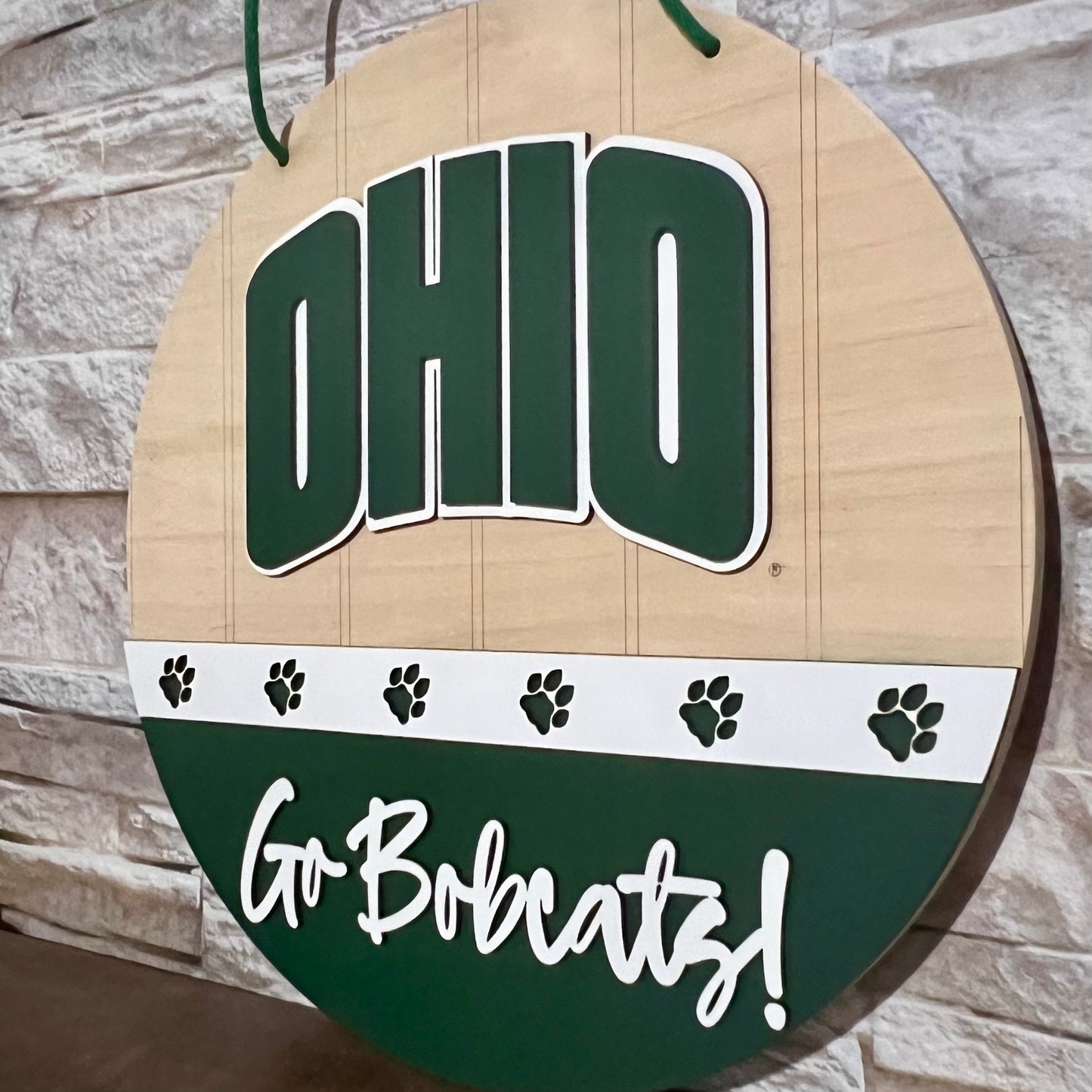 Ohio Bobcats door hanger with "Ohio" on top, a band of white with green bobcat paws across the center, and "Go Bobcats!" in white on a green lower half.