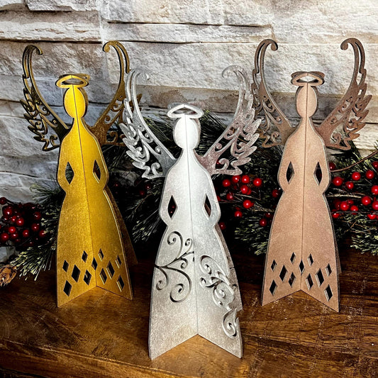 Decorative angel figurines in gold, silver, and bronze on a wooden surface with a stone wall background.